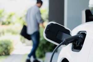 White electric vehicle being charged at home with blurred out male owner in the background. 