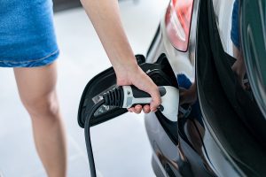 Closeup of a woman plugging in her electric vehicle to a charger at home. 