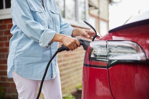 Closeup of a woman charging her red EV at home. 