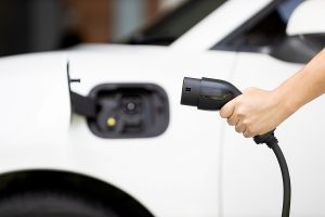 Closeup of a hand holding a plug, getting ready to charge a white electric vehicle. 