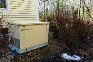 Residential standby generator outside a yellow colored home in the winter with snow on the ground.