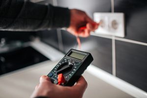 Closeup of an electrican performing an inspection by testing an electrical outlet.