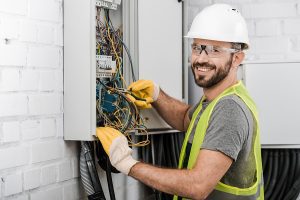 Electrician working on an electrical panel and smiling at the camera.