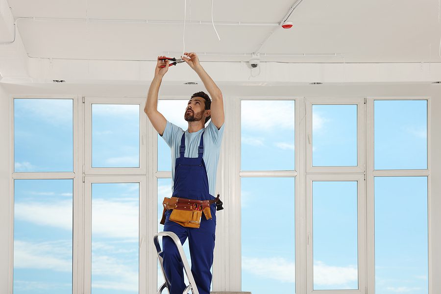 Electrician standing on a ladder working on the ceiling wiring. 