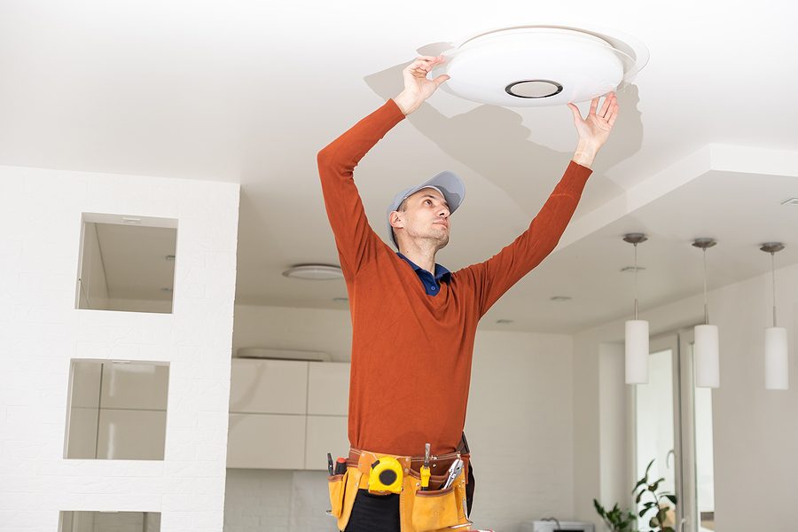 Electrician standing on a ladder replacing the lighting in a home. 