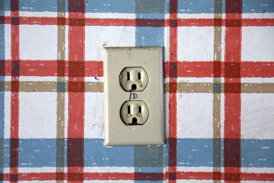 Old dangerous looking electrical outlet against plaid wall paper.